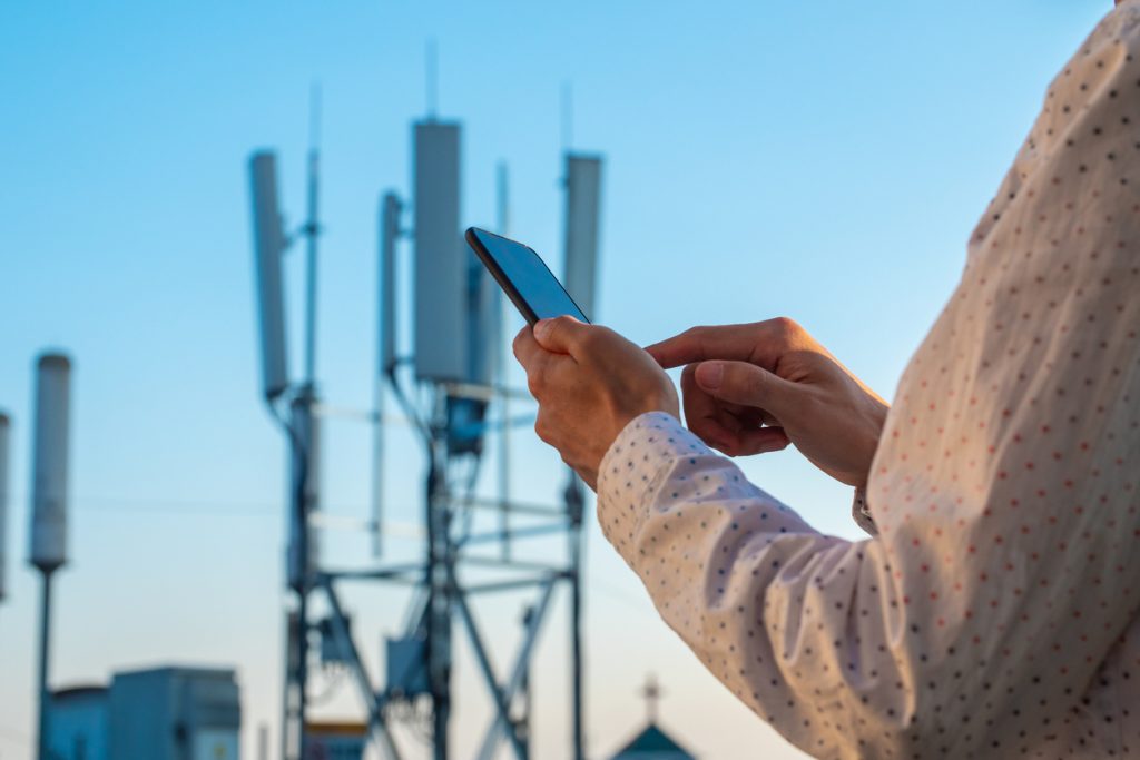 Men hand using phone with 5G telecommunications station tower background